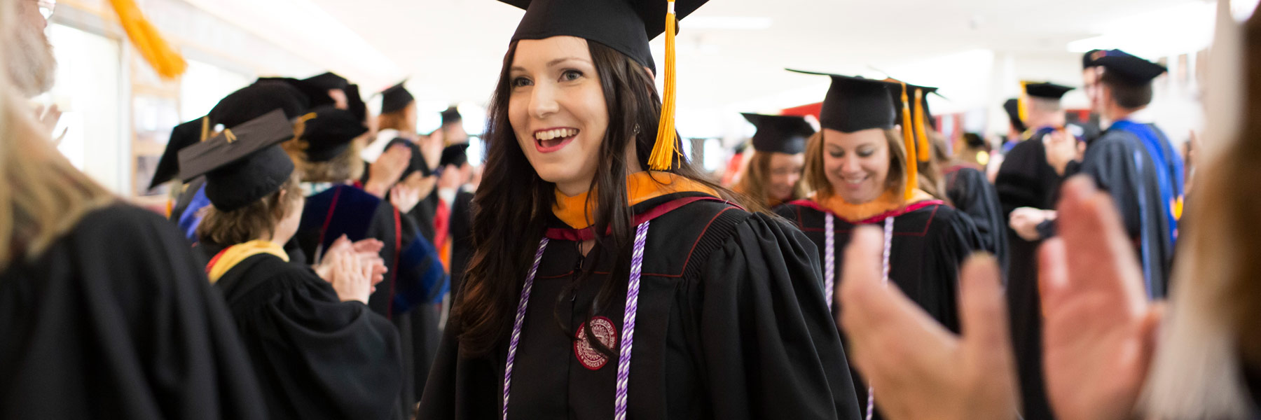 Happy female IUE graduate walking through applauding crowd.