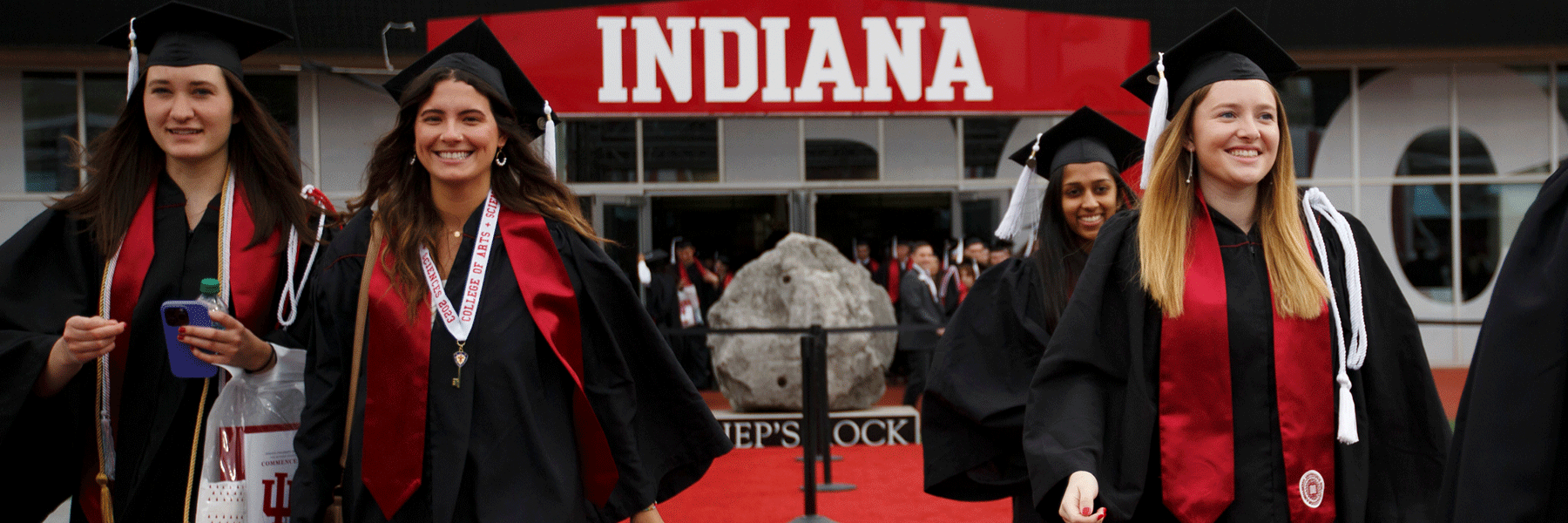Graduates walk into Memorial Stadium with Hep's Rock in the background.