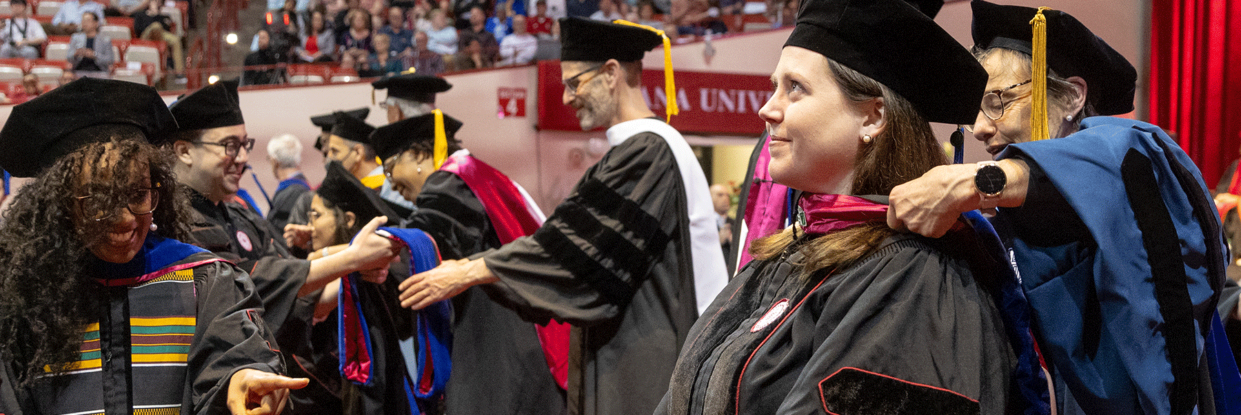 A female graduate looks up and smiles as a faculty member hoods her.