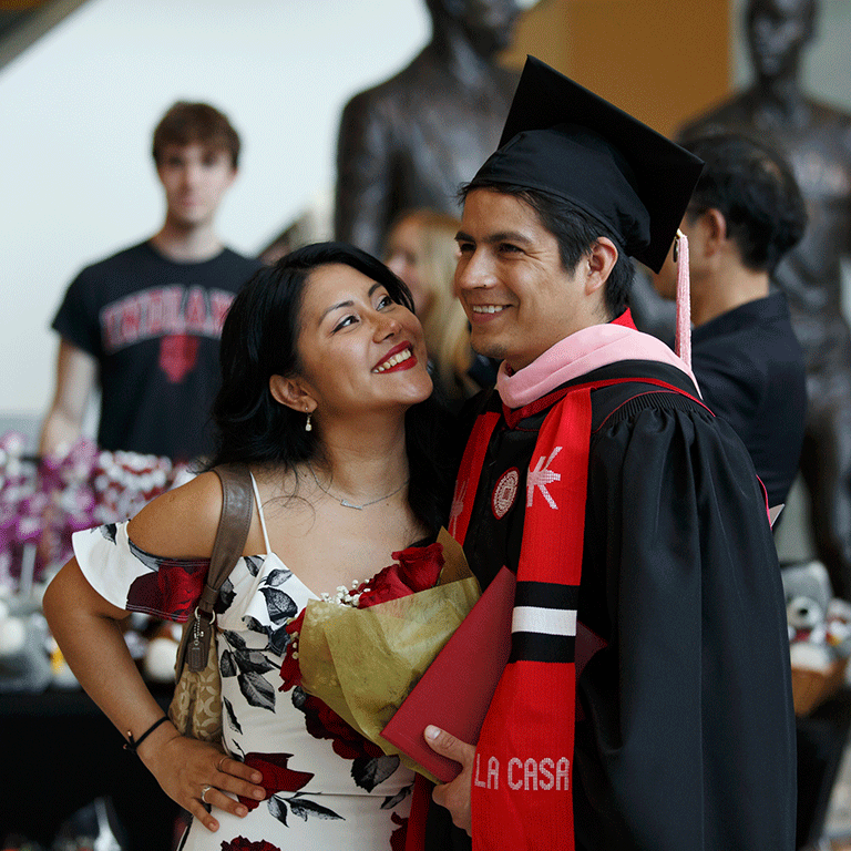 A woman in a summer dress smiles up at a new graduate.