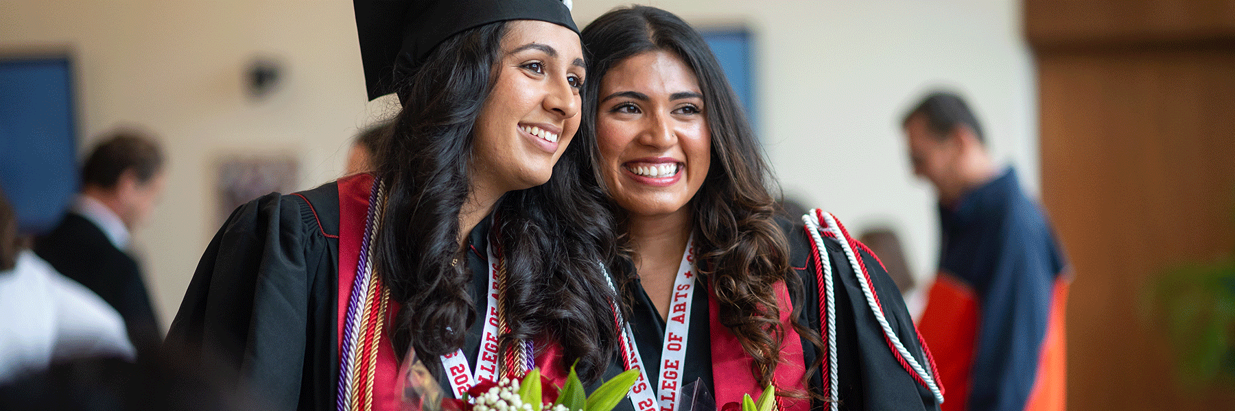 Two female graduates smiling together as they pose for a picture after commencement.