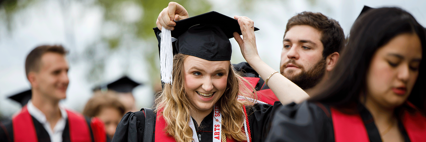 A male graduate helps a a female graduate adjusts the tassel on her graduation cap.