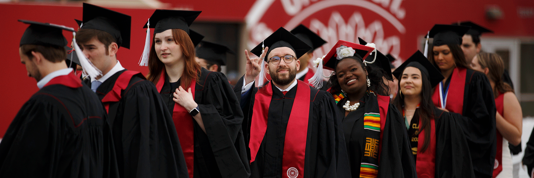 A male and female graduate smile at the camera as a group files into the commencement ceremony.