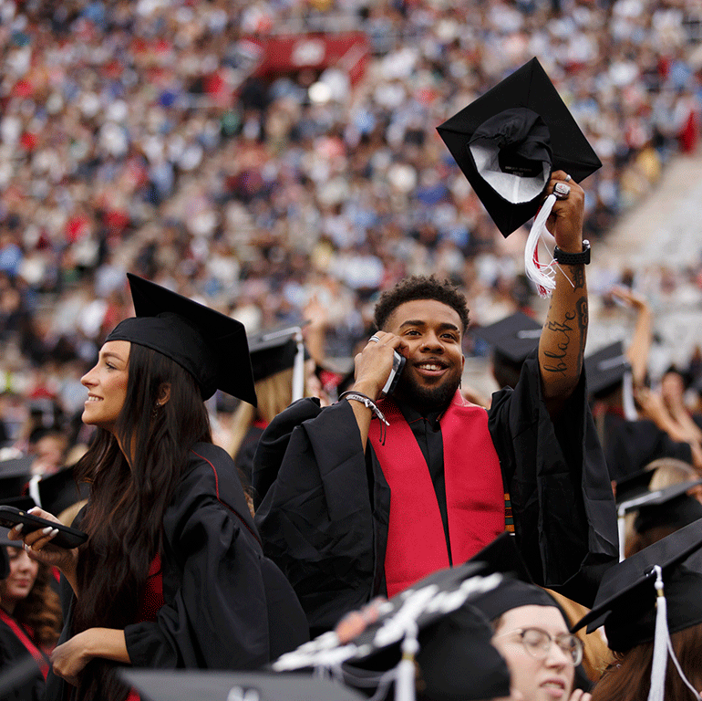 A graduate on their cell phone waves their cap.