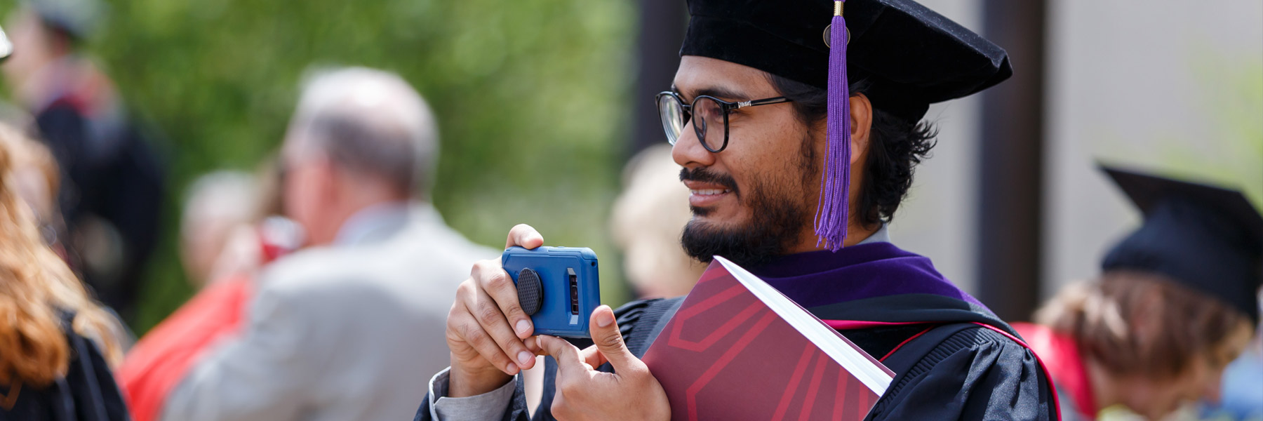 A graduate of a doctoral program holds a copy of this year's commencement program, balancing it with his cell phone as he tries to snap a pic.