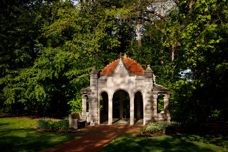 A magical image of a small ornate limestone gazebo in a lush forest (Dunn's Woods) on the IU Bloomington campus.