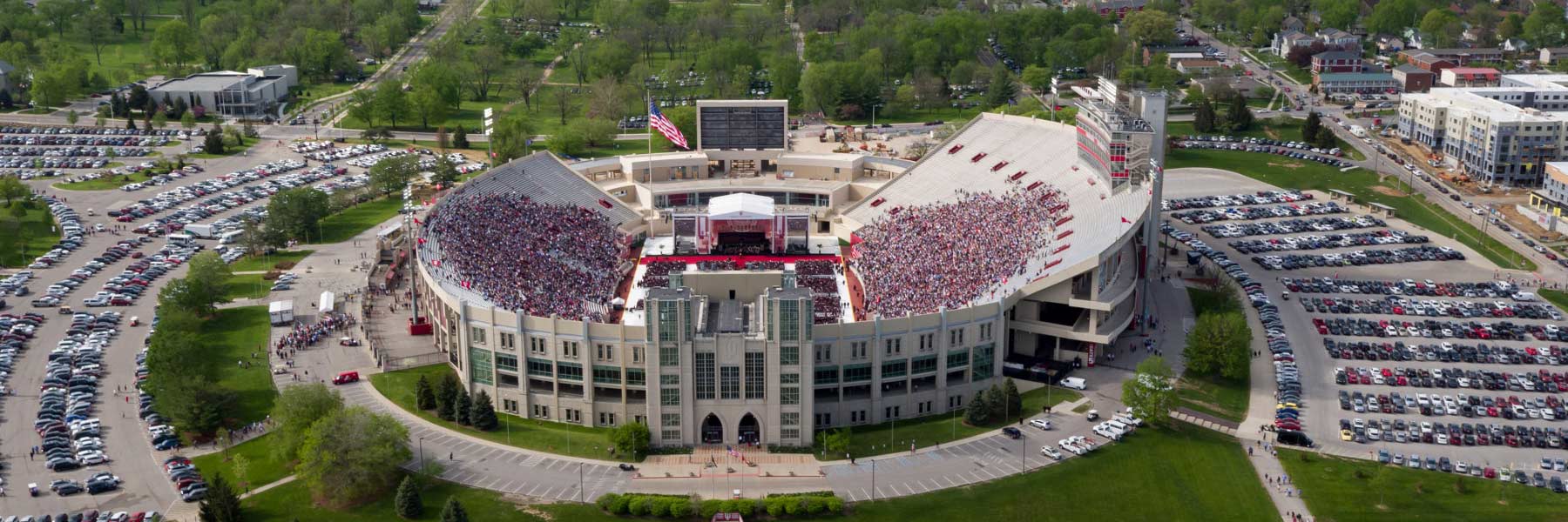 An aerial summer shot of the full stadium on the Bloomington campus at graduation, with cars crowding every available space in the surrounding parking lots. 