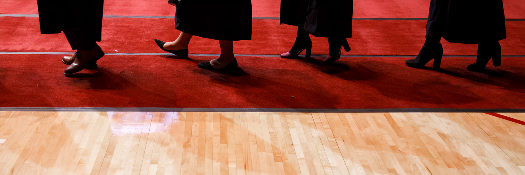 A worms'-eye-view of a line of walking graduates on red carpet.