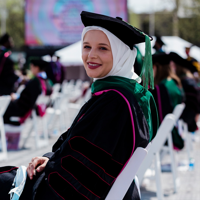 A female doctoral student, with her hair modestly covered, wears the velvet gown, tam, and doctoral hood accented with School of Medicine kelly green.