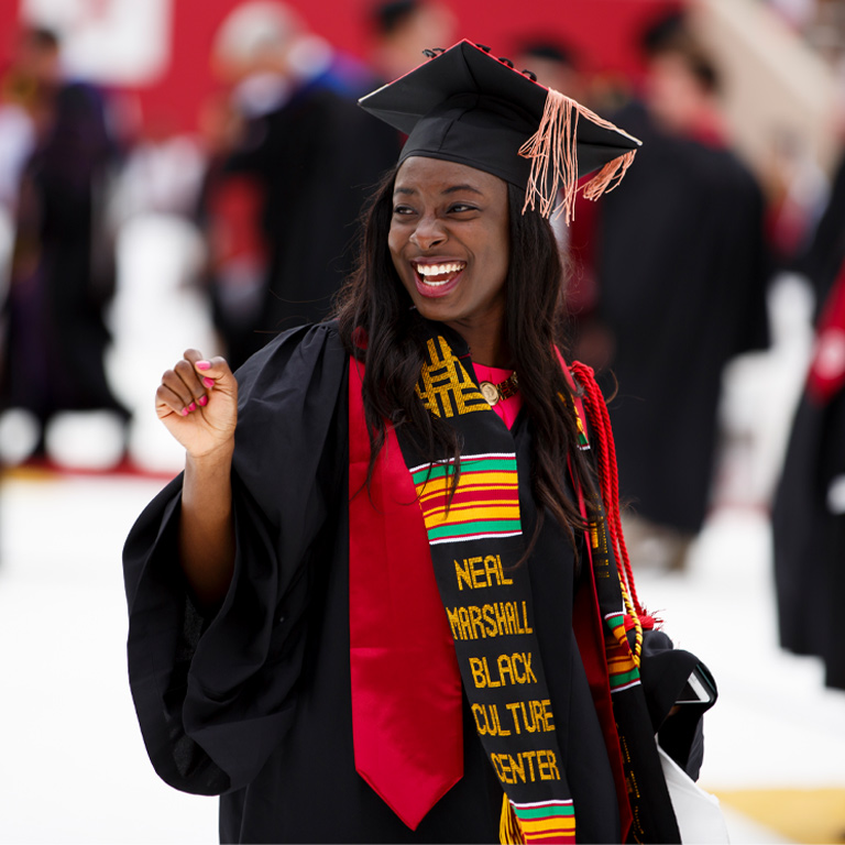 A young female graduate wearing her undergraduate gown and mortarboard, with both IU's stole of gratitude, the Neal Marshall Black Culture Center kente stole, and honor cords.