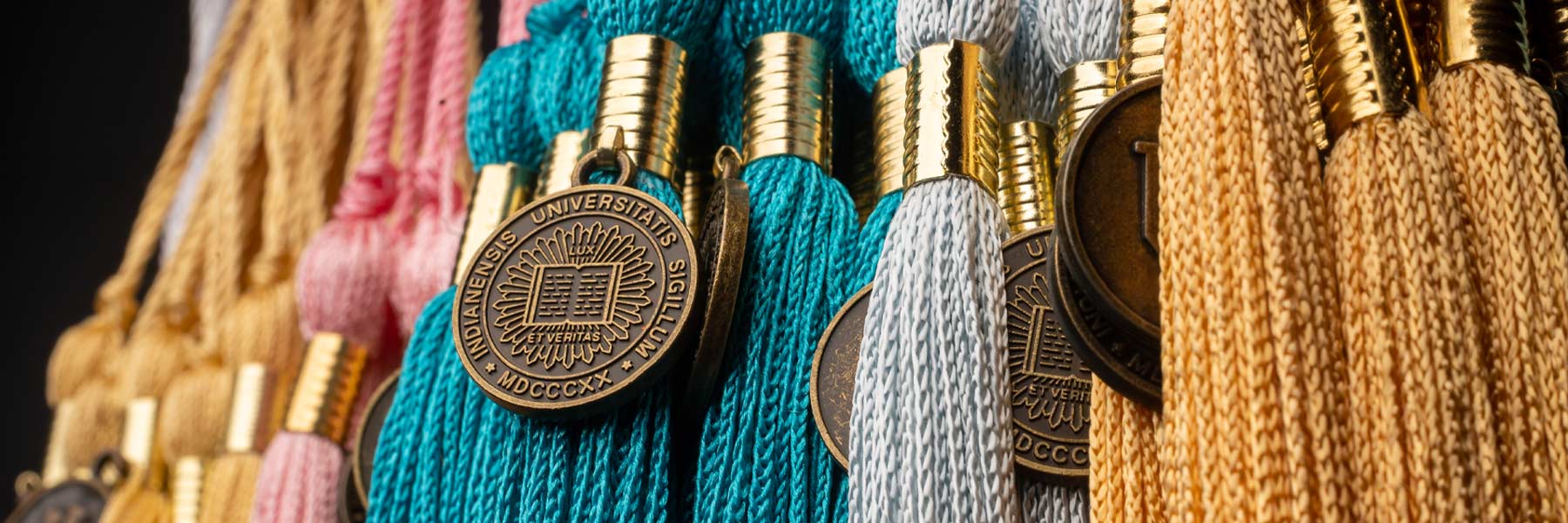 A brightly colored collection of tassels hang together in a row of turquoise, pink, bronze, gold, yellow, and blue.